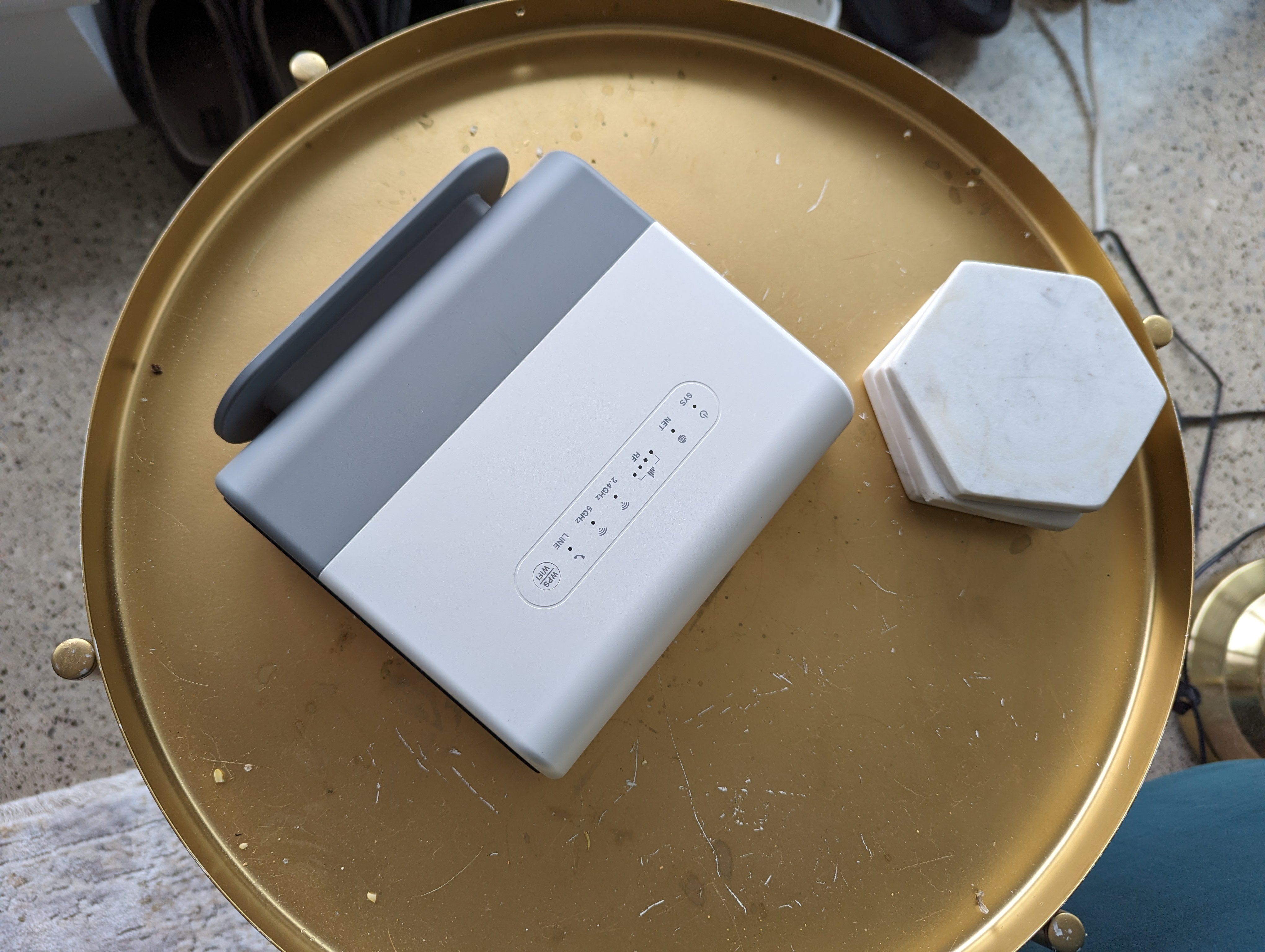 A white router with controls, next to hexagonal coasters on a round, scratched gold table.
