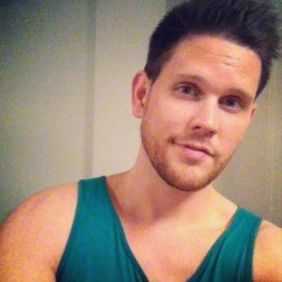 Man sitting outdoors in a brown coat, surrounded by fall foliage.