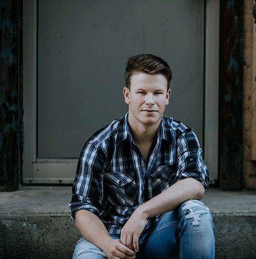 Man in plaid shirt and jeans sitting on concrete steps.