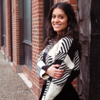 Smiling person standing against a brick wall, wearing a patterned sweater.