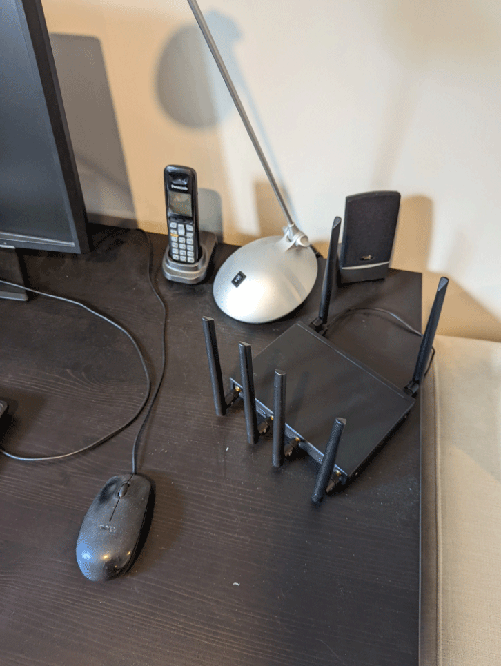 Computer desk with a wireless router, lamp, phone, and mouse.